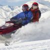 Una pareja conduce una moto de nieve en pareja (Andorra) por un paisaje nevado con las majestuosas montañas de Andorra al fondo. - ForTwo - Planes para parejas