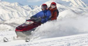 Una pareja conduce una moto de nieve en pareja (Andorra) por un paisaje nevado con las majestuosas montañas de Andorra al fondo. - ForTwo - Planes para parejas