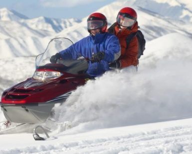 Una pareja conduce una moto de nieve en pareja (Andorra) por un paisaje nevado con las majestuosas montañas de Andorra al fondo. - ForTwo - Planes para parejas