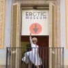 Una persona con vestido blanco y peluca saluda desde un balcón bajo el cartel de Entradas Museo Erótico de Barcelona, capturando el espíritu lúdico de la ciudad. - ForTwo - Planes para parejas