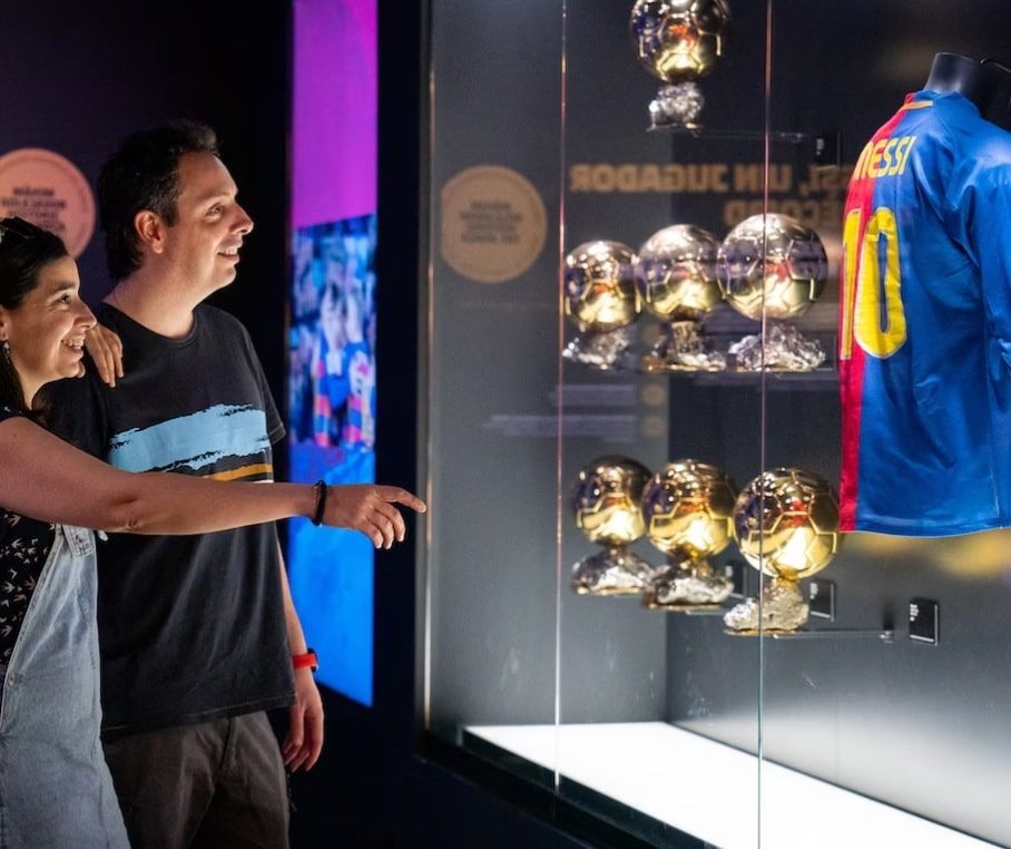 Dos visitantes admiran una exposición de trofeos dorados y una camiseta azul y roja con el número 10 en el Museo del Barça, disfrutando de un inolvidable Tour Inmersivo. - ForTwo - Planes para parejas