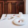 La elegante mesa del Restaurante Novodabo de Zaragoza muestra su exquisito Menú degustación con un plato blanco, una jarra pequeña, cubiertos y guarniciones sobre un mantel impecable entre cálidas paredes de madera. - ForTwo - Planes para parejas