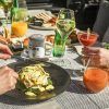 Manos disfrutando del Brunch de Fin de Semana: saborea huevos Benedict, jugos frescos, cócteles y platos variados en un mantel texturizado en Only YOU Hotel Atocha en Madrid. - ForTwo - Planes para parejas