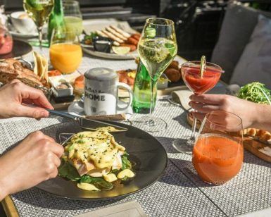 Manos disfrutando del Brunch de Fin de Semana: saborea huevos Benedict, jugos frescos, cócteles y platos variados en un mantel texturizado en Only YOU Hotel Atocha en Madrid. - ForTwo - Planes para parejas