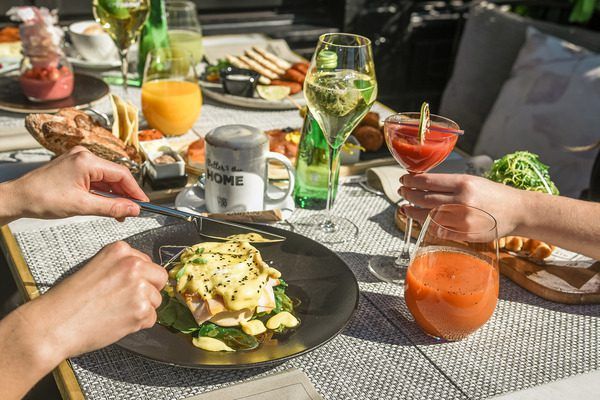 Manos disfrutando del Brunch de Fin de Semana: saborea huevos Benedict, jugos frescos, cócteles y platos variados en un mantel texturizado en Only YOU Hotel Atocha en Madrid. - ForTwo - Planes para parejas