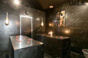 Experimente el lujoso Baño turco para parejas en Madrid (Hammam Vital Experience), con paredes de mármol oscuro, elegantes mesas, lámparas colgantes y pétalos de rosa. El ambiente sereno y el cautivador retrato mural lo convierten en el lugar perfecto para relajarse como nunca antes. - ForTwo - Planes para parejas