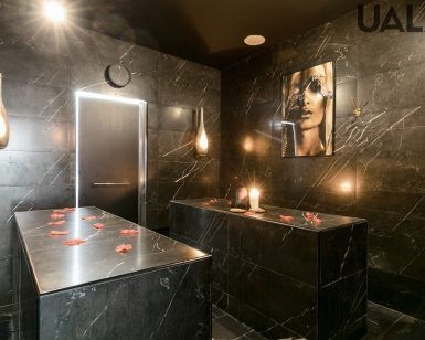 Experimente el lujoso Baño turco para parejas en Madrid (Hammam Vital Experience), con paredes de mármol oscuro, elegantes mesas, lámparas colgantes y pétalos de rosa. El ambiente sereno y el cautivador retrato mural lo convierten en el lugar perfecto para relajarse como nunca antes. - ForTwo - Planes para parejas