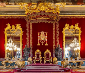 La gran sala del trono refleja el esplendor del Palacio Real de Madrid con sus paredes rojas, decoración dorada, dos tronos, grandes espejos, candelabros y estatuas de leones. Descubre esta elegancia con "Entradas para Madrid: Visita de día completo con entrada rápida al Museo del Prado y al Palacio Real. - ForTwo - Planes para parejas