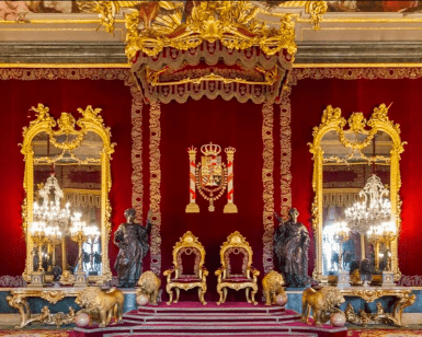 La gran sala del trono refleja el esplendor del Palacio Real de Madrid con sus paredes rojas, decoración dorada, dos tronos, grandes espejos, candelabros y estatuas de leones. Descubre esta elegancia con "Entradas para Madrid: Visita de día completo con entrada rápida al Museo del Prado y al Palacio Real. - ForTwo - Planes para parejas
