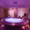 Una pareja se relaja en un jacuzzi circular rodeado de velas encendidas en una sala de spa tenuemente iluminada, evocando el ambiente sereno de la experiencia del "Circuito termal de spa con masaje, té, chocolate y fruta" en Tenerife. - ForTwo - Planes para parejas