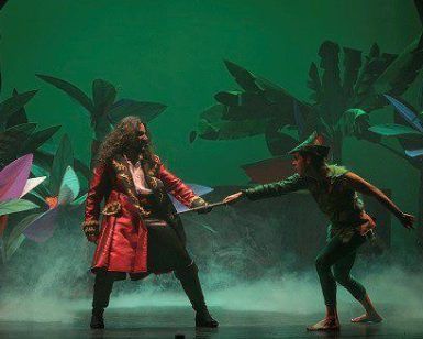 Actores con trajes coloridos dramatizan una escena en el escenario del Teatro Maravillas, rodeados de plantas vibrantes, dando vida a la magia de "Peter Pan, el musical". - ForTwo - Planes para parejas