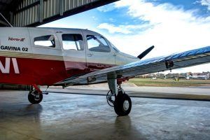 En un hangar, una pequeña avioneta roja y blanca espera, con las puntas de sus alas brillando a la luz del sol. Perfectamente preparada para el "Vuelo en avioneta a Barcelona", imagina el emocionante viaje por los vibrantes paisajes de Barcelona. - ForTwo - Planes para parejas