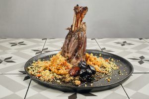 El Menú Al Ándalus del Restaurante Carmen El Agua (Granada) ofrece una pierna de cordero magníficamente presentada, complementada con cuscús, verduras y ciruelas pasas, celebrando la herencia culinaria de Granada. - ForTwo - Planes para parejas