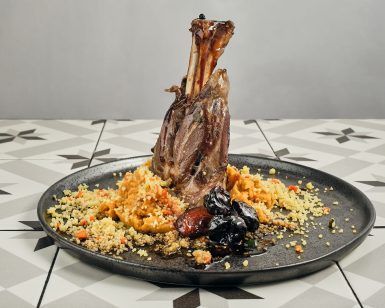 El Menú Al Ándalus del Restaurante Carmen El Agua (Granada) ofrece una pierna de cordero magníficamente presentada, complementada con cuscús, verduras y ciruelas pasas, celebrando la herencia culinaria de Granada. - ForTwo - Planes para parejas