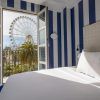 El Hotel Room Mate Valeria Málaga ofrece una encantadora habitación con paredes de rayas azules y puertas de balcón abiertas, que ofrecen una vista impresionante de una noria y palmeras. - ForTwo - Planes para parejas