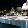 Cene elegantemente en el Restaurante Abades Triana con una mesa preparada para seis personas, disfrutando de una vista nocturna del paisaje urbano iluminado y la histórica Torre de Triana. - ForTwo - Planes para parejas