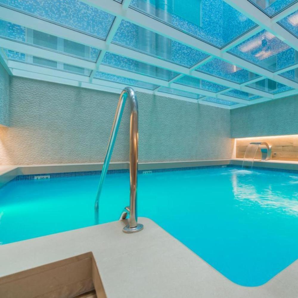 Una tranquila piscina cubierta de agua turquesa, bajo un techo de cristal y una iluminación suave, crea un ambiente de spa sereno en el Circuito de Spa & Masaje del Hotel Sallés Pere IV, Barcelona. - ForTwo - Planes para parejas