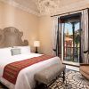 Descubra la máxima elegancia en la Suite Deluxe del Hotel Alfonso XIII de Sevilla. Disfrute de una espaciosa habitación con una cama grande, lámpara de araña y sillón, mientras admira las impresionantes vistas a una histórica torre enmarcada por frondosas palmeras desde la ventana. - ForTwo - Planes para parejas