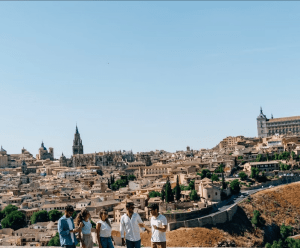 Cinco personas paseando disfrutan de una impresionante vista de los edificios históricos de Madrid bajo un cielo azul claro, que recuerda a escenas de "Madrid y Toledo: Excursión guiada de un día y Museo del Prado". - ForTwo - Planes para parejas