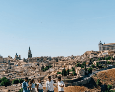 Cinco personas paseando disfrutan de una impresionante vista de los edificios históricos de Madrid bajo un cielo azul claro, que recuerda a escenas de "Madrid y Toledo: Excursión guiada de un día y Museo del Prado". - ForTwo - Planes para parejas