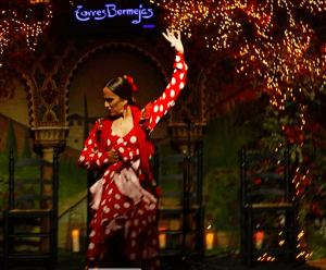 Una bailaora de flamenco con un llamativo vestido rojo y blanco actúa con pasión en el Tablao Flamenco Torres Bermejas, donde una cálida iluminación realza cada movimiento. - ForTwo - Planes para parejas