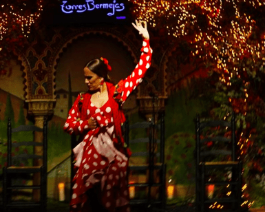 Una bailaora de flamenco con un llamativo vestido rojo y blanco actúa con pasión en el Tablao Flamenco Torres Bermejas, donde una cálida iluminación realza cada movimiento. - ForTwo - Planes para parejas