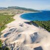 Experimente Zahara de los Atunes con dunas doradas que se fusionan con bosques verdes a lo largo de su costa curva de color turquesa, frente a montañas distantes en la "Visita por la Costa de Tarifa, Zahara de los Atunes y Baelo Claudia (Cádiz)". - ForTwo - Planes para parejas