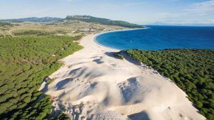 Experimente Zahara de los Atunes con dunas doradas que se fusionan con bosques verdes a lo largo de su costa curva de color turquesa, frente a montañas distantes en la "Visita por la Costa de Tarifa, Zahara de los Atunes y Baelo Claudia (Cádiz)". - ForTwo - Planes para parejas