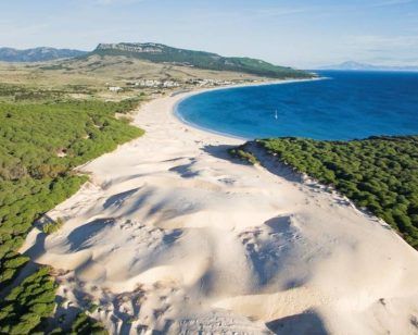 Experimente Zahara de los Atunes con dunas doradas que se fusionan con bosques verdes a lo largo de su costa curva de color turquesa, frente a montañas distantes en la "Visita por la Costa de Tarifa, Zahara de los Atunes y Baelo Claudia (Cádiz)". - ForTwo - Planes para parejas