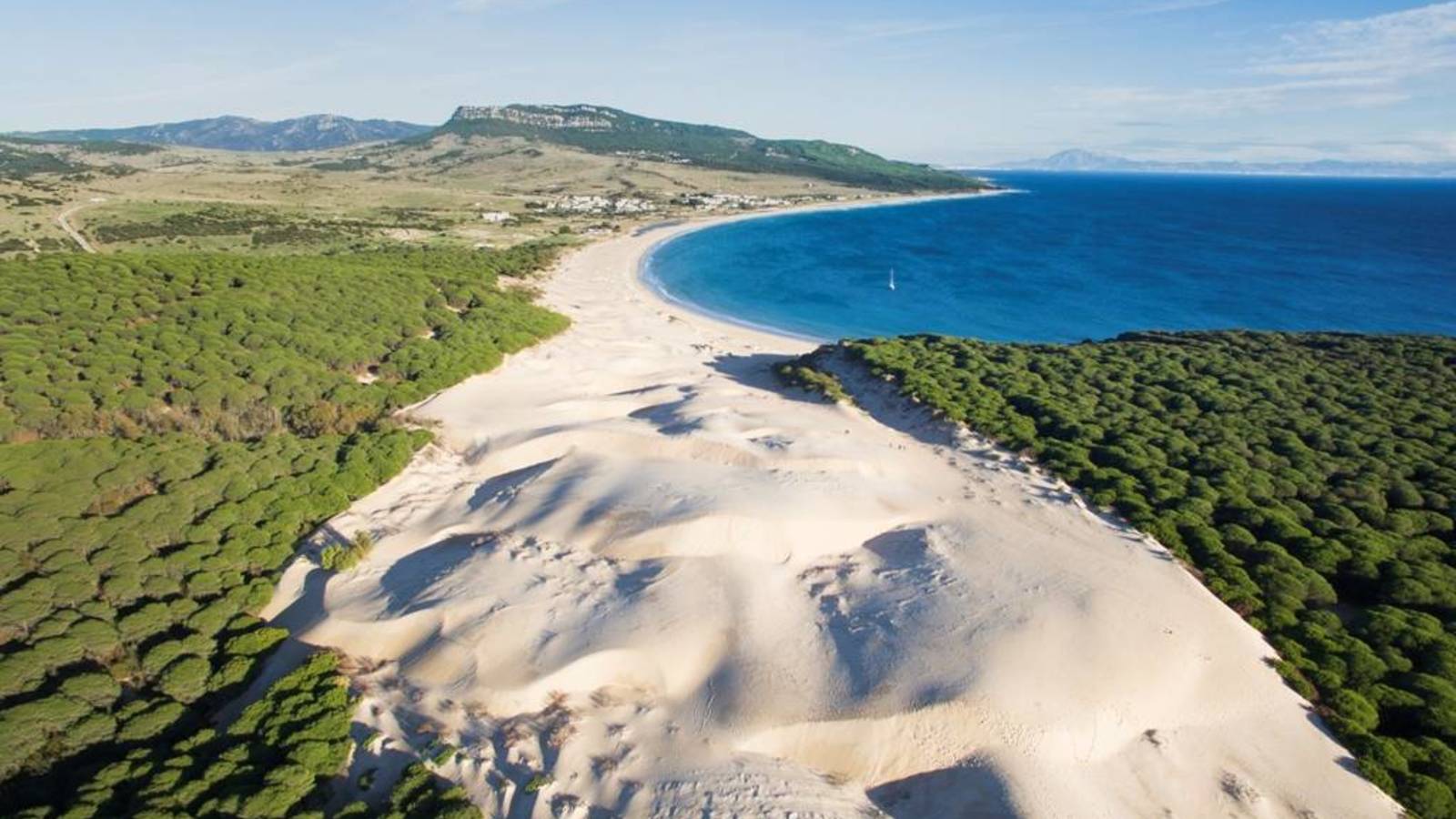 Experimente Zahara de los Atunes con dunas doradas que se fusionan con bosques verdes a lo largo de su costa curva de color turquesa, frente a montañas distantes en la "Visita por la Costa de Tarifa, Zahara de los Atunes y Baelo Claudia (Cádiz)". - ForTwo - Planes para parejas