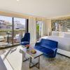 Descubra la elegancia del Hotel The One Barcelona GL, que cuenta con una espaciosa habitación con una cama grande, asientos azules y puertas de cristal que se abren a un balcón con impresionantes vistas a la ciudad. - ForTwo - Planes para parejas
