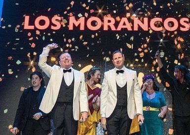 Los artistas en el escenario bajo el cartel "Todo por la Matria - Los Morancos (Madrid)", vestidos con trajes formales y rodeados de cascadas de confeti, capturan el espíritu vibrante de Madrid. - ForTwo - Planes para parejas