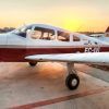 Una pequeña avióneta roja y blanca está estacionada en una pista al atardecer, lista para un Vuelo de iniciación en avióneta por Montserrat (Barcelona) sobre el impresionante paisaje. - ForTwo - Planes para parejas