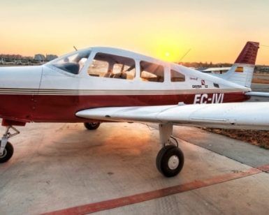 Una pequeña avióneta roja y blanca está estacionada en una pista al atardecer, lista para un Vuelo de iniciación en avióneta por Montserrat (Barcelona) sobre el impresionante paisaje. - ForTwo - Planes para parejas