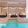 Lujosa sala de spa con dos camas con dosel junto a la piscina, con elegantes cortinas e iluminación ambiental; ideal para un "Masaje en pareja con técnicas de relajación profunda y acceso al spa" en Yurbban Passage Hotel & Spa, Barcelona. - ForTwo - Planes para parejas