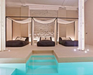 Lujosa sala de spa con dos camas con dosel junto a la piscina, con elegantes cortinas e iluminación ambiental; ideal para un "Masaje en pareja con técnicas de relajación profunda y acceso al spa" en Yurbban Passage Hotel & Spa, Barcelona. - ForTwo - Planes para parejas