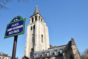 Placa de calle de la Place Saint-Germain des Prés con la torre de la iglesia al fondo bajo un cielo azul claro, que recuerda el encanto que se encuentra en un "Recorrido guiado por el Barrio Latino" gratuito en París. - ForTwo - Planes para parejas