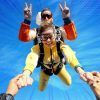 Paracaidistas tándem con vibrantes trajes amarillos se elevan alegremente con su instructor bajo un cielo azul despejado. ¡Vive la emoción del "Paracaidismo tándem desde 4000 metros" en SkyDive Madrid!. - ForTwo - Planes para parejas