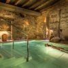 En una piscina de hidromasaje cubierta con poca luz, paredes de piedra y decoración rústica, uno puede disfrutar del relajante lujo del "Baño termal con aromaterapia y masaje de 15 minutos por Aire de Vallromanes" en Barcelona. - ForTwo - Planes para parejas