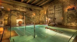 En una piscina de hidromasaje cubierta con poca luz, paredes de piedra y decoración rústica, uno puede disfrutar del relajante lujo del "Baño termal con aromaterapia y masaje de 15 minutos por Aire de Vallromanes" en Barcelona. - ForTwo - Planes para parejas