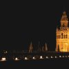 La torre gótica iluminada se eleva contra el oscuro cielo nocturno, sus detalles ornamentados bañados de luz, recuerdan el resplandor sereno de un Hammam sencillo en Aire de Sevilla. - ForTwo - Planes para parejas