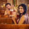 Dos personas en Granada disfrutan del Circuito Beer Spa Privado Premium, compartiendo sonrisas mientras una vierte cerveza de un grifo en recipientes de madera, con una pared de ladrillos rústicos como telón de fondo. - ForTwo - Planes para parejas