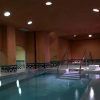 Como parte de la "OFERTA: Circuito en Baños Árabes para 2 con cava, bombones y masaje opcional", la piscina cubierta con poca luz cuenta con escalones rodeados de cálidas paredes marrones y azulejos decorativos. - ForTwo - Planes para parejas