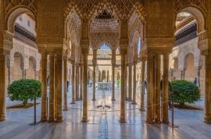 Explore el ornamentado patio de la Alhambra de Granada, con intrincados arcos y columnas enmarcados por arbustos verdes alrededor de una fuente central. Disfrute de un ambiente tranquilo bajo un cielo despejado con la "Visita guiada a la Alhambra con entrada incluida" para apreciar plenamente esta maravilla arquitectónica. - ForTwo - Planes para parejas