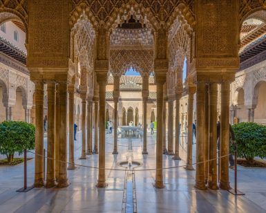 Explore el ornamentado patio de la Alhambra de Granada, con intrincados arcos y columnas enmarcados por arbustos verdes alrededor de una fuente central. Disfrute de un ambiente tranquilo bajo un cielo despejado con la "Visita guiada a la Alhambra con entrada incluida" para apreciar plenamente esta maravilla arquitectónica. - ForTwo - Planes para parejas