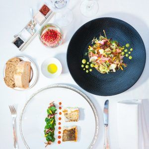 Un elegante montaje gastronómico para el "Masaje y almuerzo ejecutivo a la carta en el Hotel InterContinental Gran Vía (Madrid)" presenta dos platos gourmet, pan, aceite de oliva y condimentos sobre un mantel blanco impecable, perfecto para una experiencia refinada. - ForTwo - Planes para parejas