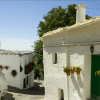 Descubre el encanto de la Alpujarra en "Alpujarra: Tour guiado desde Granada". Pasea entre casas de estuco blanco con puertas verdes y macetas con flores a lo largo de una calle soleada y arbolada para disfrutar de la auténtica belleza andaluza. - ForTwo - Planes para parejas