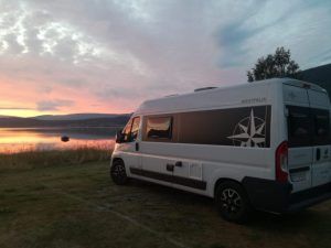 Una Catalunyavan, bajo un vibrante atardecer junto a un tranquilo lago con colinas a lo lejos, invita a explorar más allá de Barcelona. Ideal para quienes buscan "Alquiler de furgos camperizadas con Catalunyavan (Barcelona)" y sumergirse en la serena belleza de la naturaleza. - ForTwo - Planes para parejas