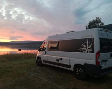 Una Catalunyavan, bajo un vibrante atardecer junto a un tranquilo lago con colinas a lo lejos, invita a explorar más allá de Barcelona. Ideal para quienes buscan "Alquiler de furgos camperizadas con Catalunyavan (Barcelona)" y sumergirse en la serena belleza de la naturaleza. - ForTwo - Planes para parejas