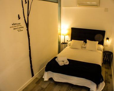 Acogedor dormitorio en Apartamento para 2 en el centro de Granada con cama de matrimonio, dos lámparas pequeñas, arte de pared y toallas dobladas sobre la colcha. - ForTwo - Planes para parejas